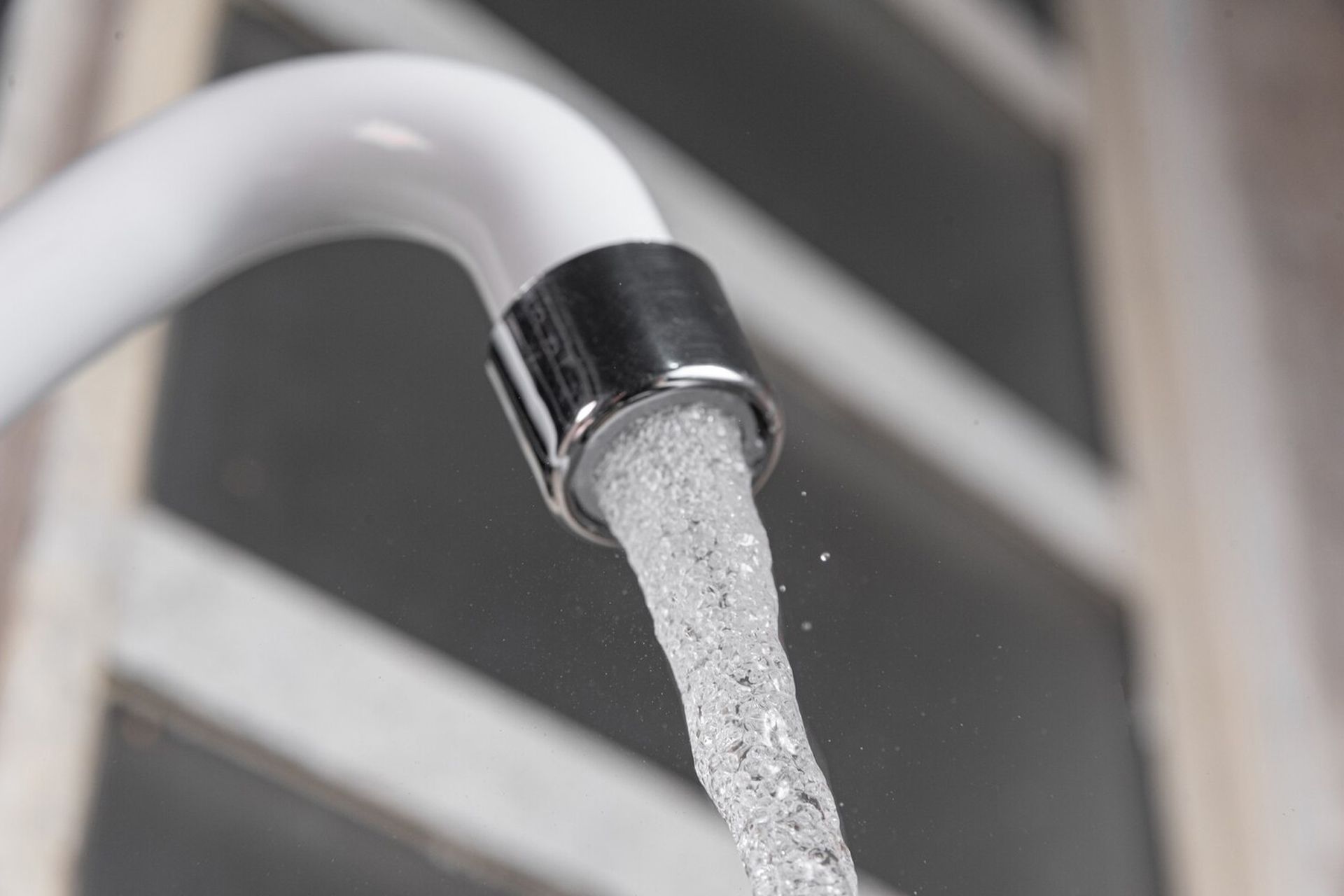 White faucet with running water, close-up.  Window in background.