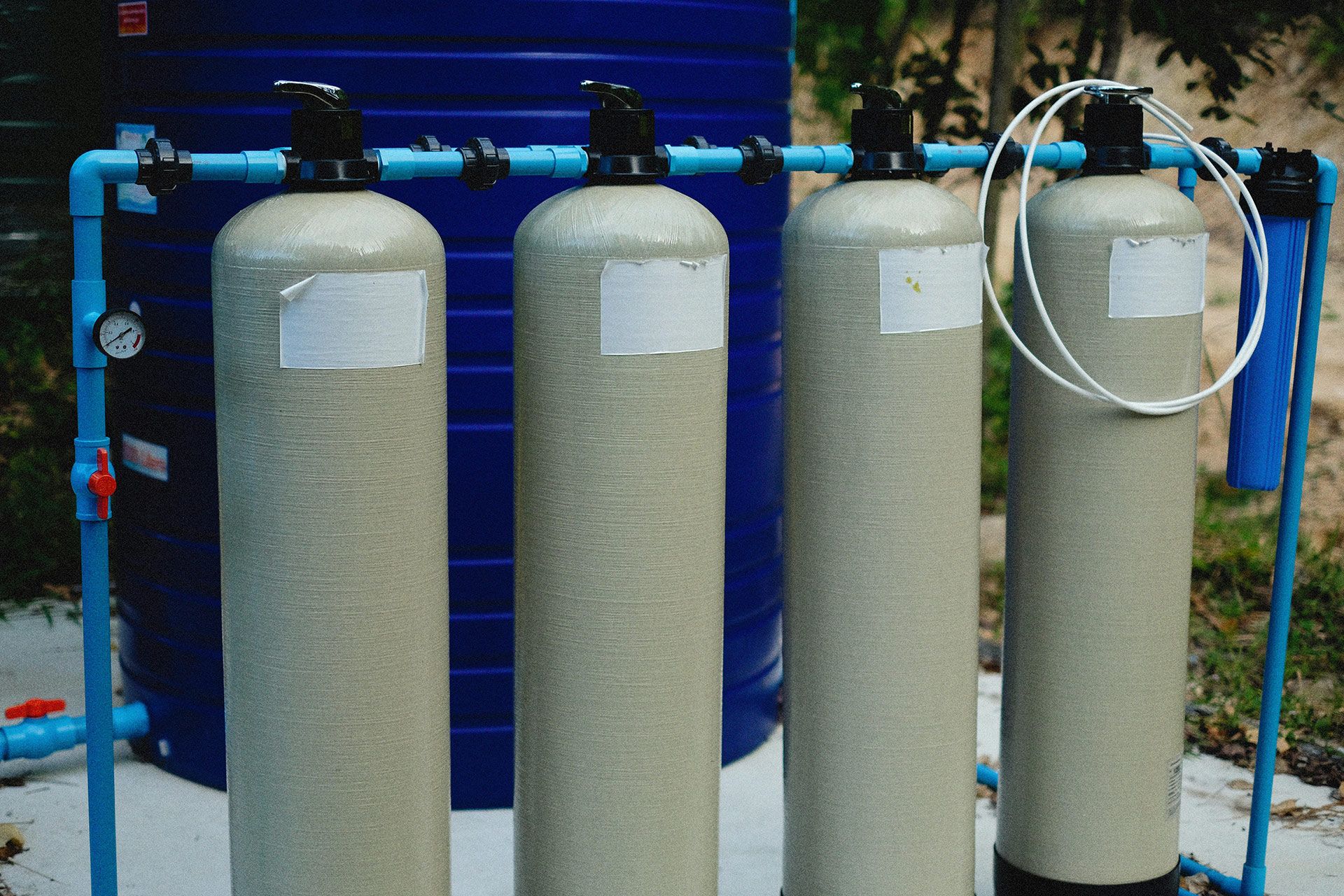 Four beige water filtration tanks connected by blue pipes, next to a blue water tank.
