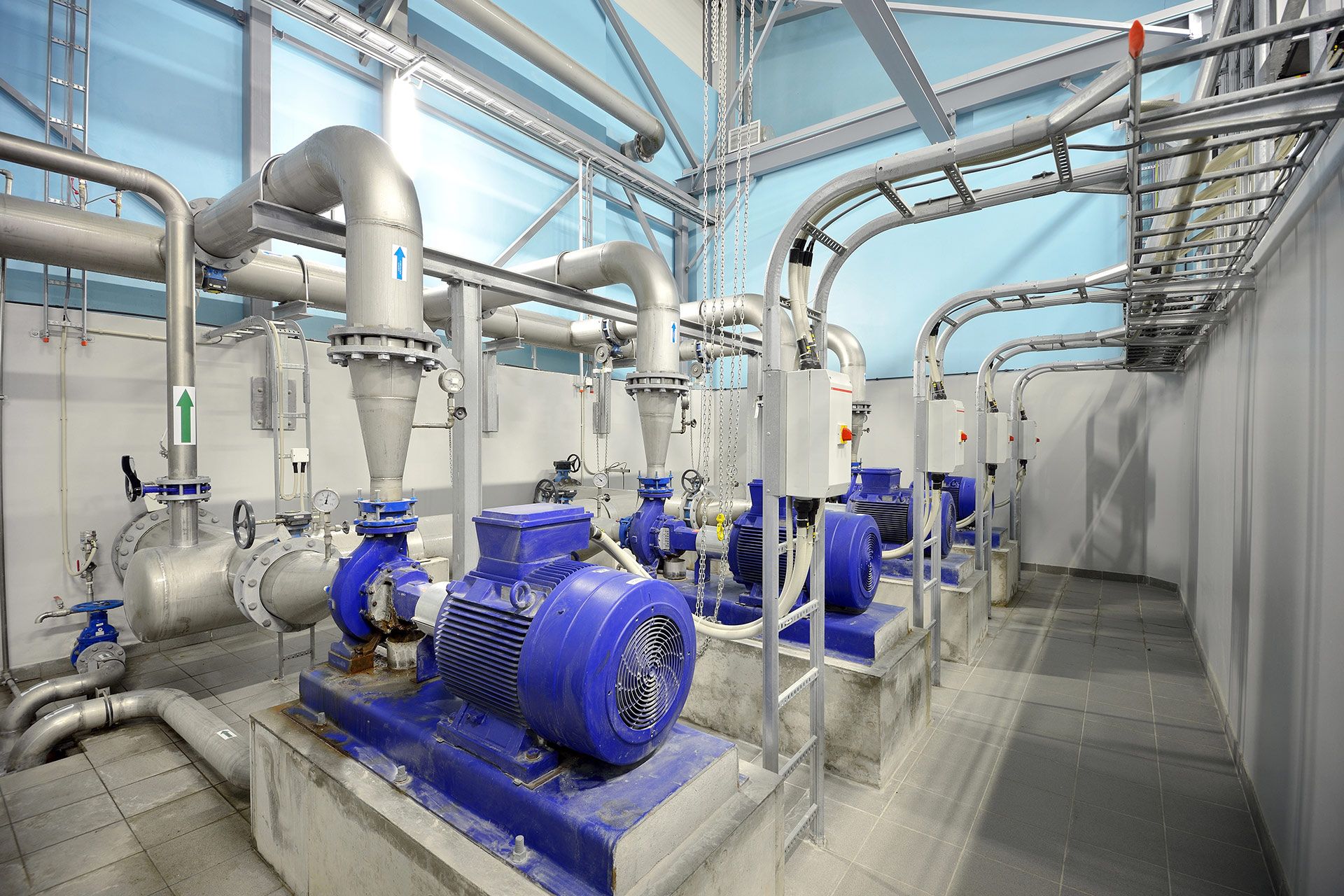 Blue water pumps in a utility room with silver pipes and conduits along the ceiling.