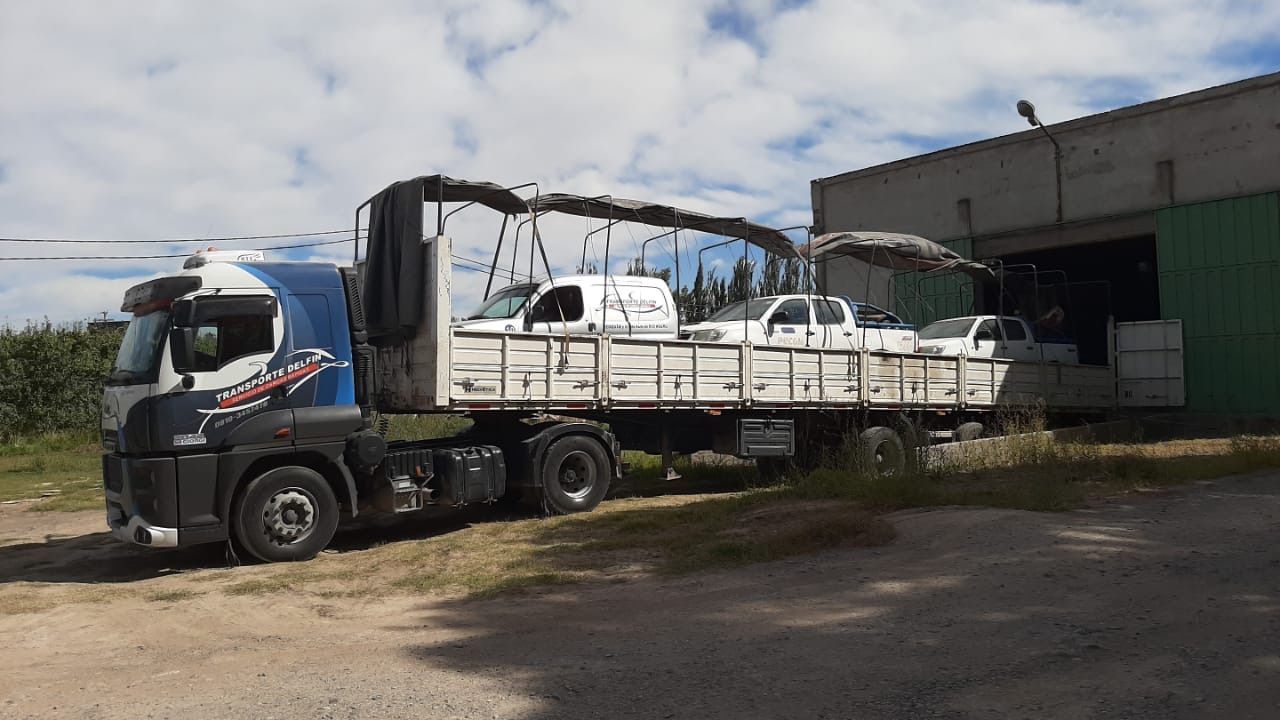 Un camión azul estacionado junto a un almacén transportaba una carga de plataforma con materiales cubiertos de blanco.