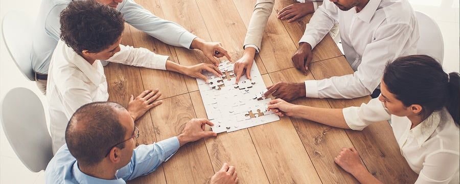 Turn Collaboration into Action A group of people working together to solve a jigsaw puzzle on a wooden table.