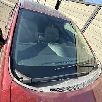 A red car with a broken windshield is parked in a parking lot.