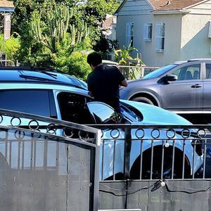 A man is standing next to a blue car in a parking lot.