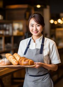 A woman is holding a tray of bread in a bakery.