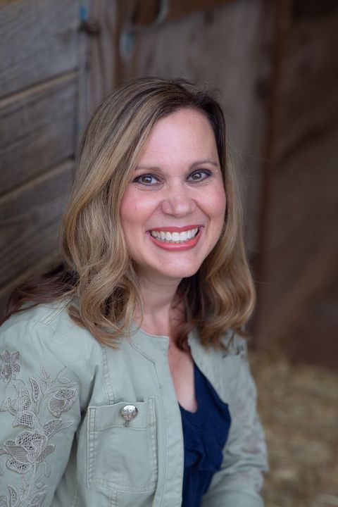 Smiling woman in a blue denim jacket against a light outdoor background