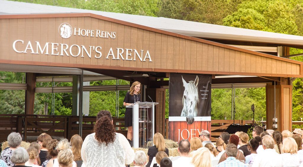 Crowd gathered outside Cameron's Arena stage under a wooden canopy with a banner and horse image