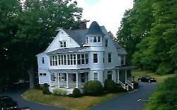 White Victorian house with porch, surrounded by trees, beside a driveway