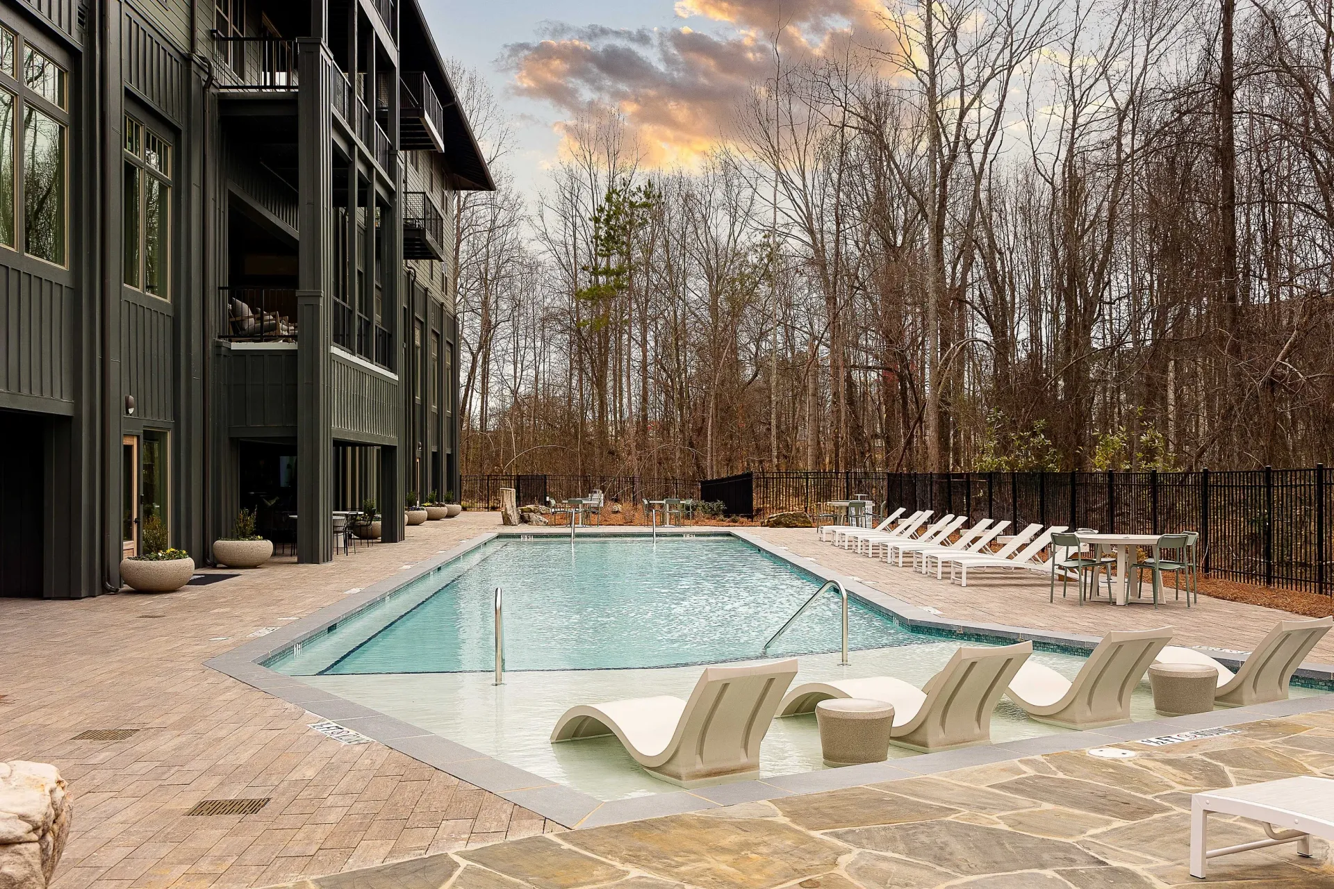 Outdoor swimming pool area with lounge chairs and tables next to a modern apartment building.