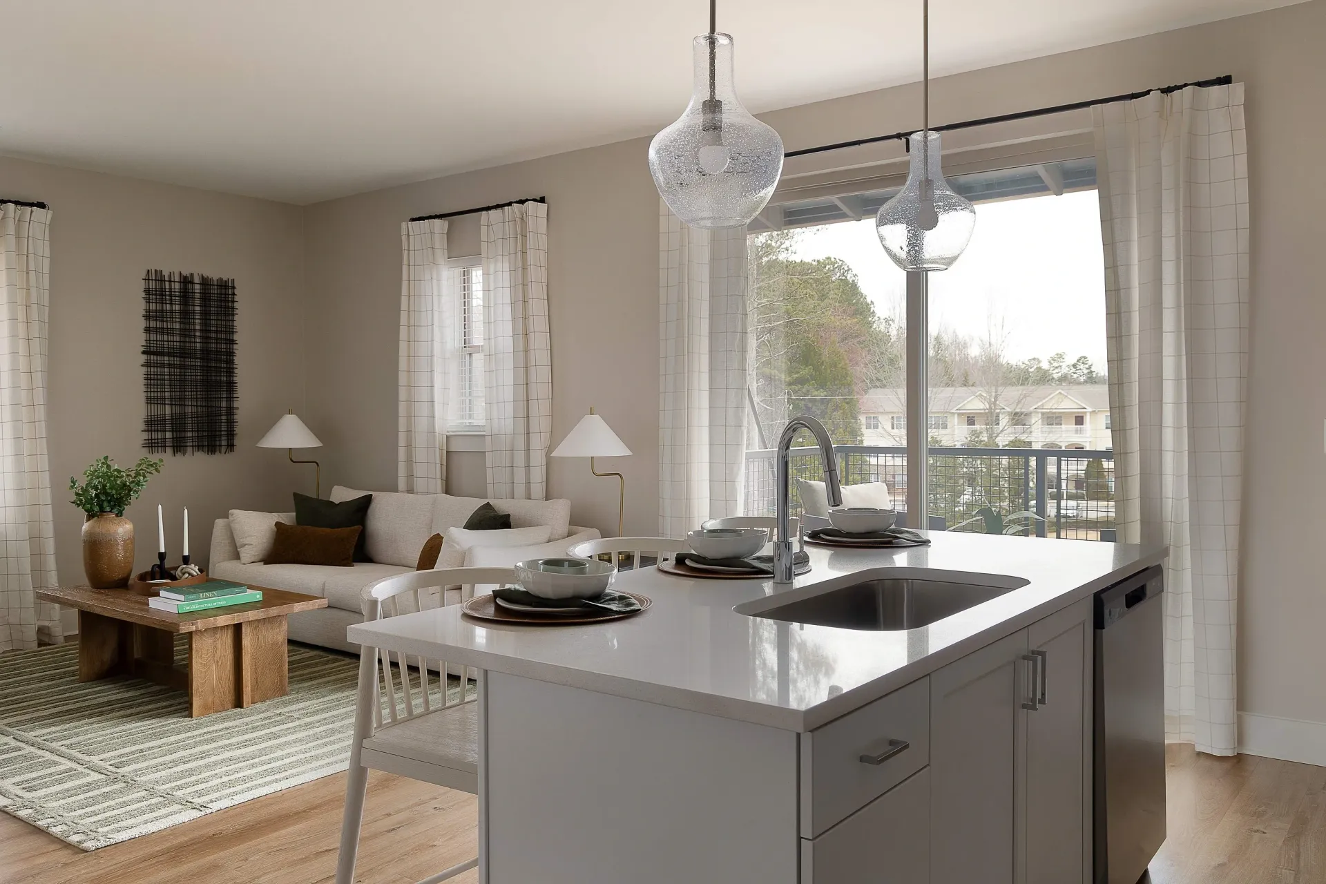 Modern kitchen island with sink and stainless steel dishwasher, adjacent to living room with couch and coffee table.