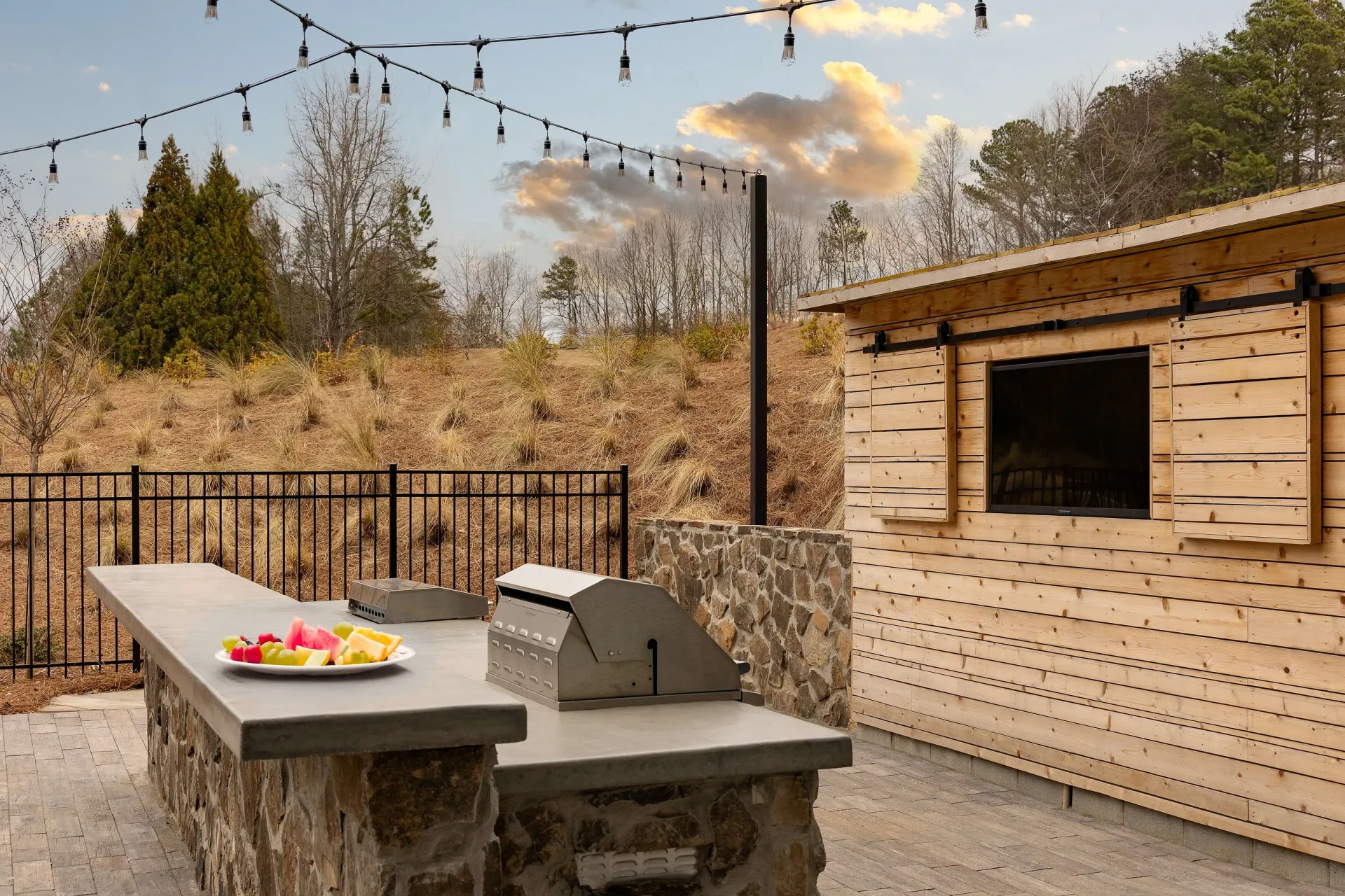 Outdoor kitchen area with a built-in grill and serving counter, string lights overhead.
