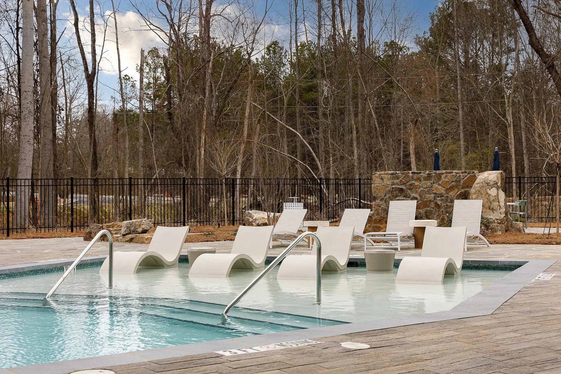 Modern swimming pool with in-water loungers and surrounding lounge chairs.