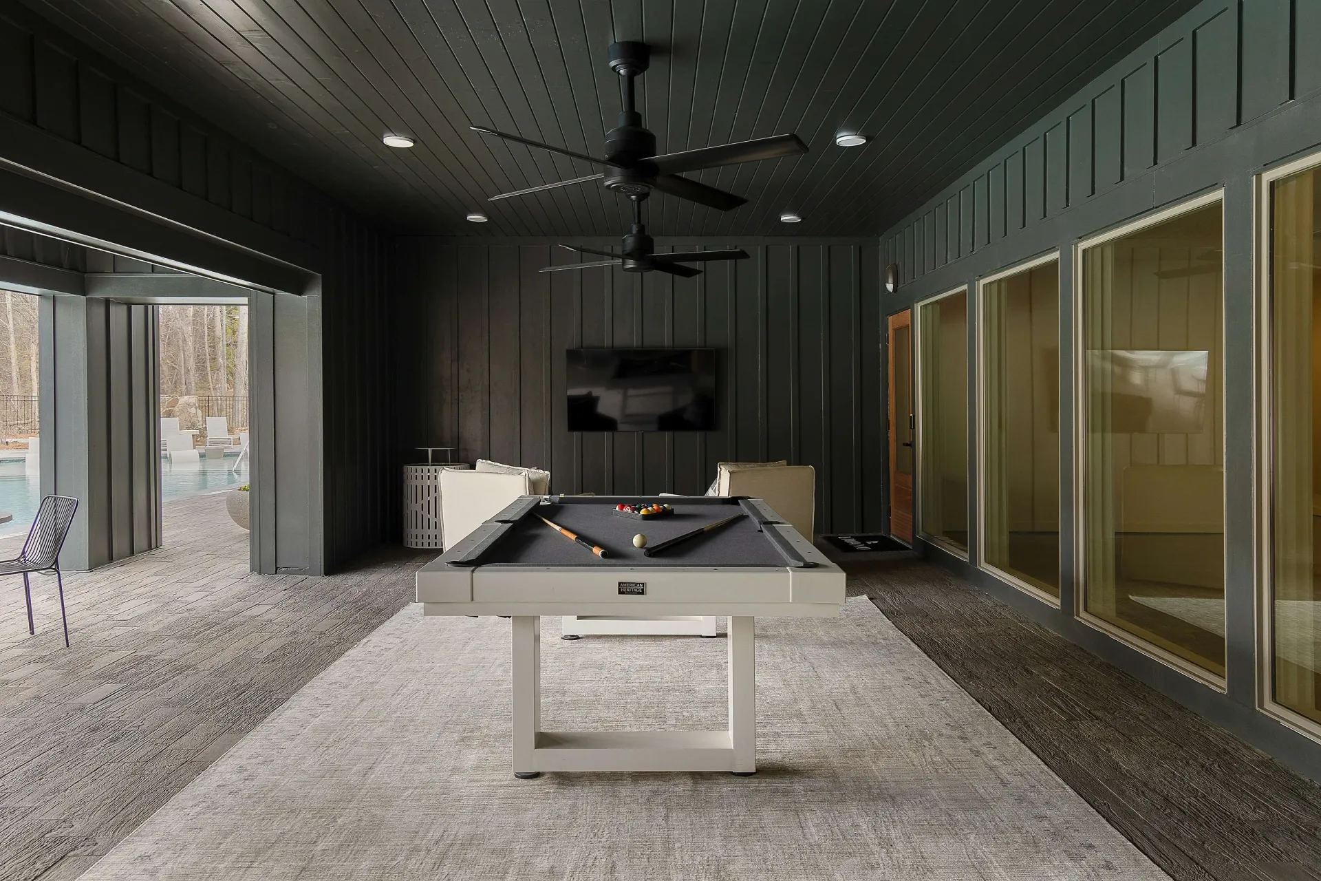 Modern game room with a pool table and view of the outdoor pool area.