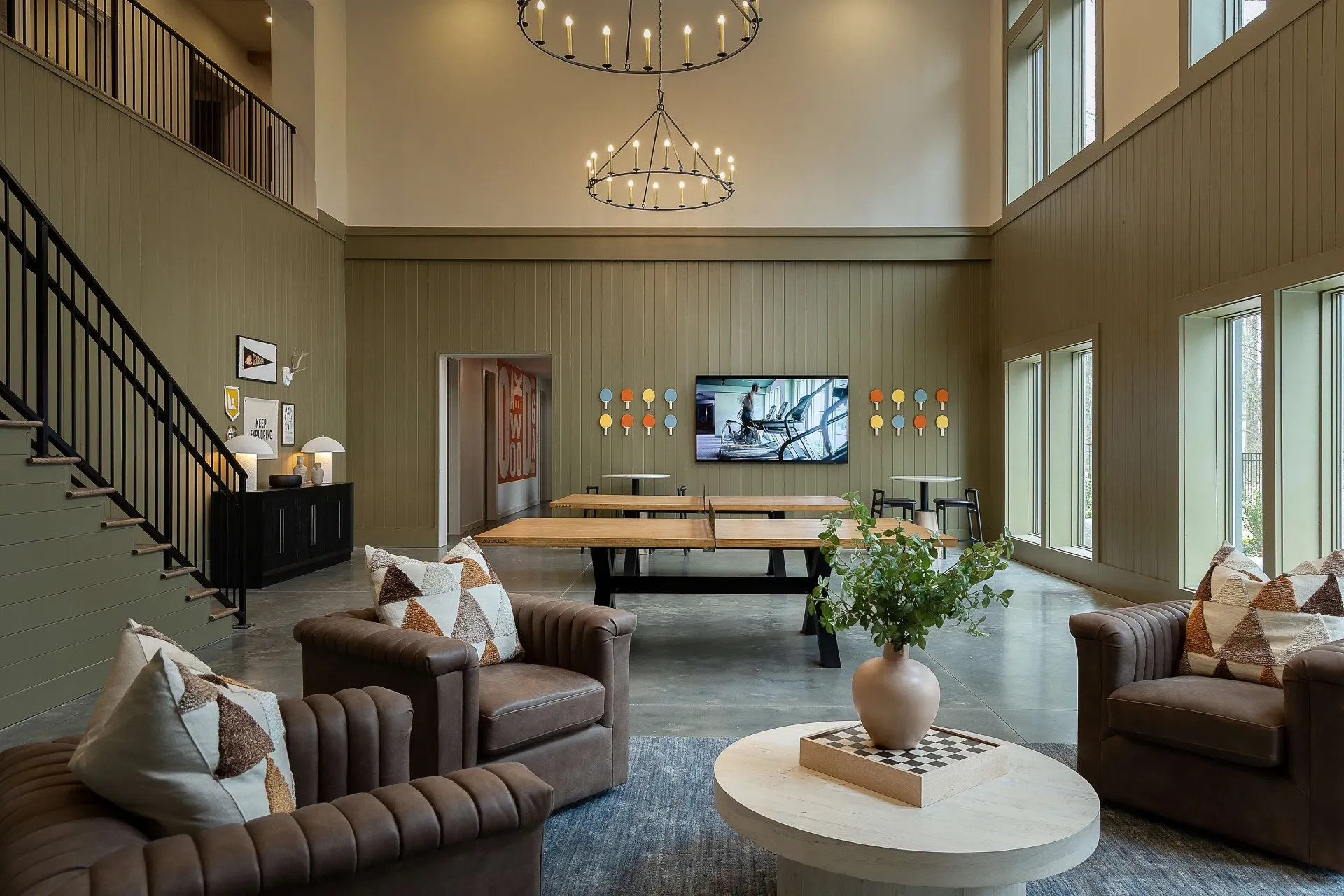 Community lounge with seating, ping pong table, and large screen TV displaying a treadmill.