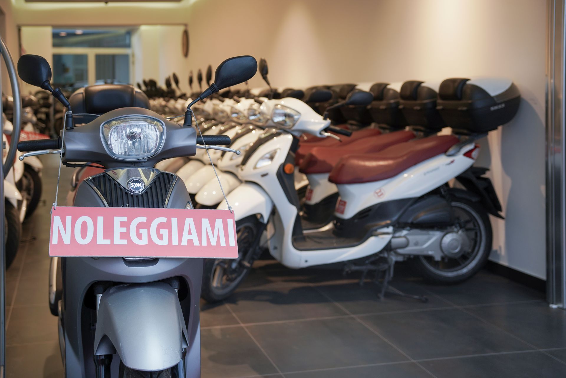 Una fila di scooter sono parcheggiati in una stanza con un cartello che dice noleggiami