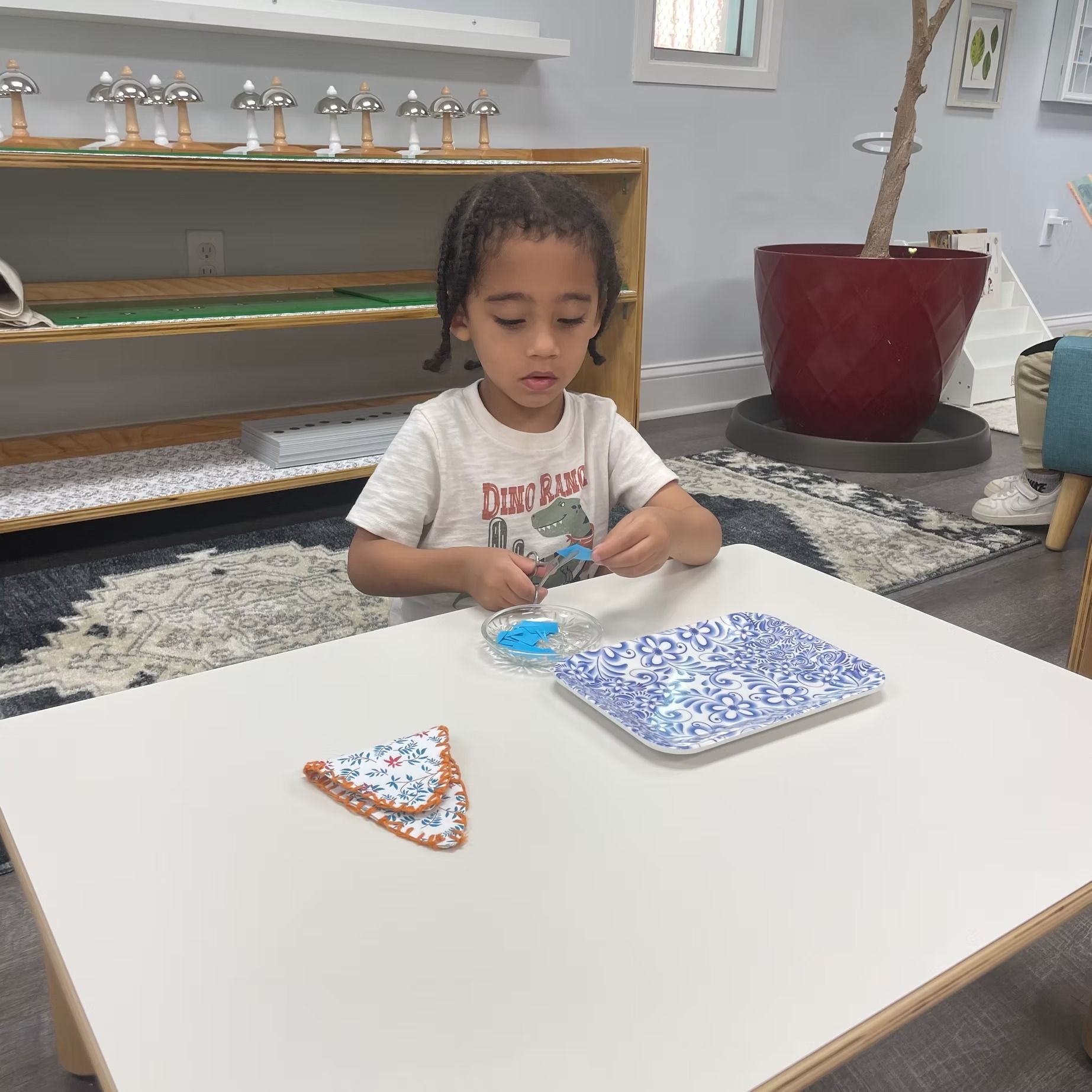 Child at a table playing with small blue and orange pieces in a living room.