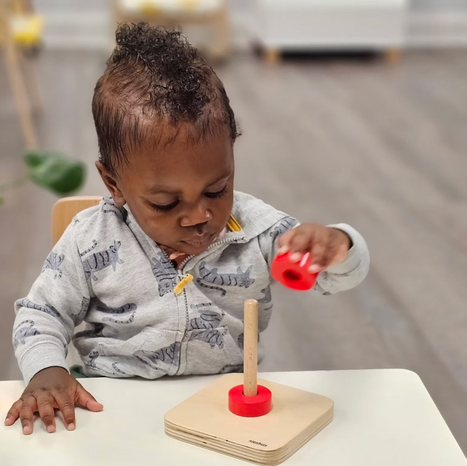 Toddler placing a red ring onto a wooden stacking toy at a table