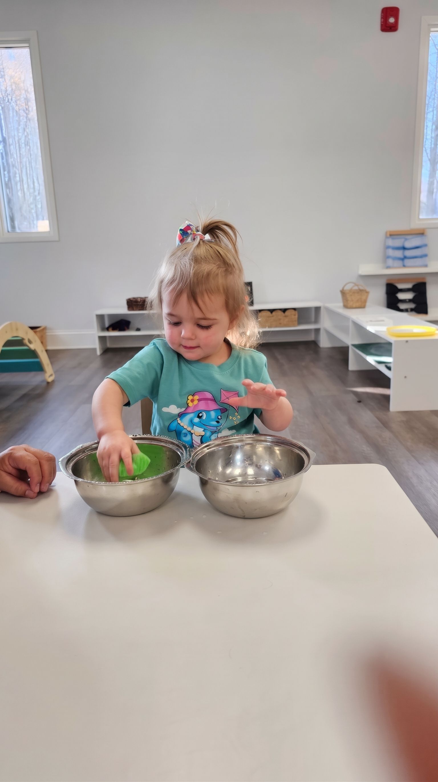 Child mixing ingredients in a metal bowl at a table in a bright classroom