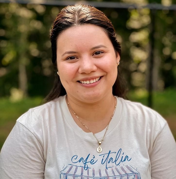 Smiling person in a white T-shirt standing outdoors with blurred greenery in the background