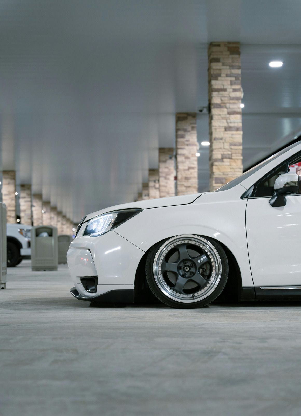 Lowered white sports car parked in a concrete garage with brick columns