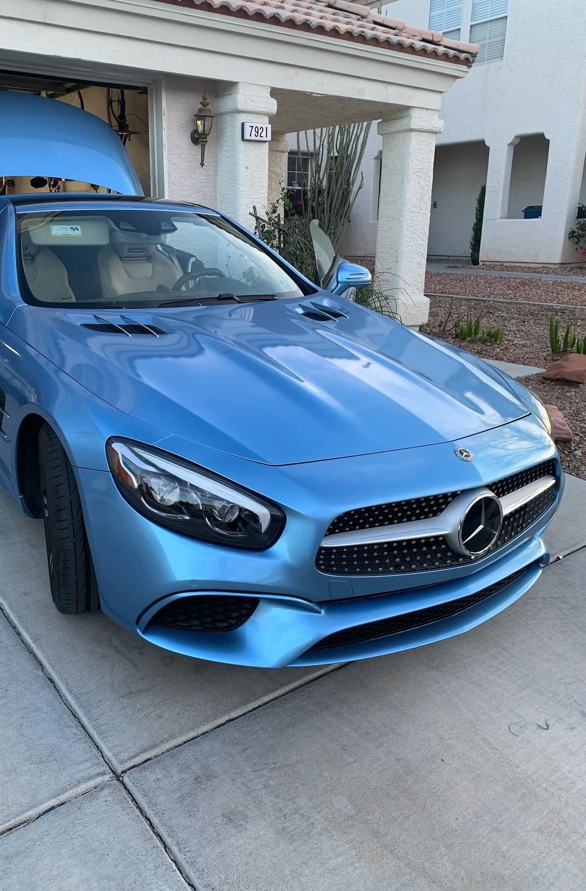 Blue Mercedes-Benz parked in a driveway outside a stucco house with a tiled roof.