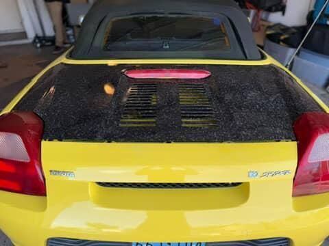 Yellow sports car with a black rear engine cover and pink accent, parked in a garage