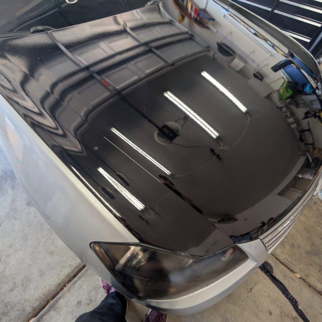 Shiny black car hood reflecting garage lights and ceiling