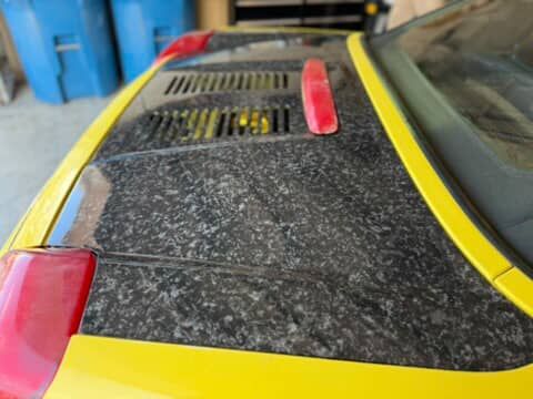 Dusty black car hood with yellow trim and red vent covers in a garage