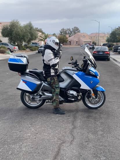 Motorcyclist standing beside a blue-and-white touring motorcycle on a suburban street