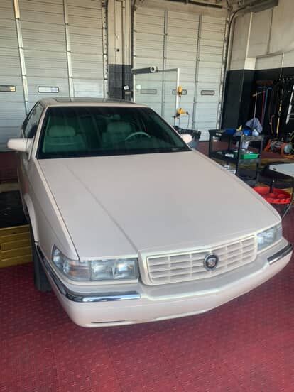 White sedan parked inside a garage with a red floor and workshop tools nearby