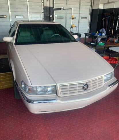 White Cadillac sedan parked inside a garage with a red carpeted floor.