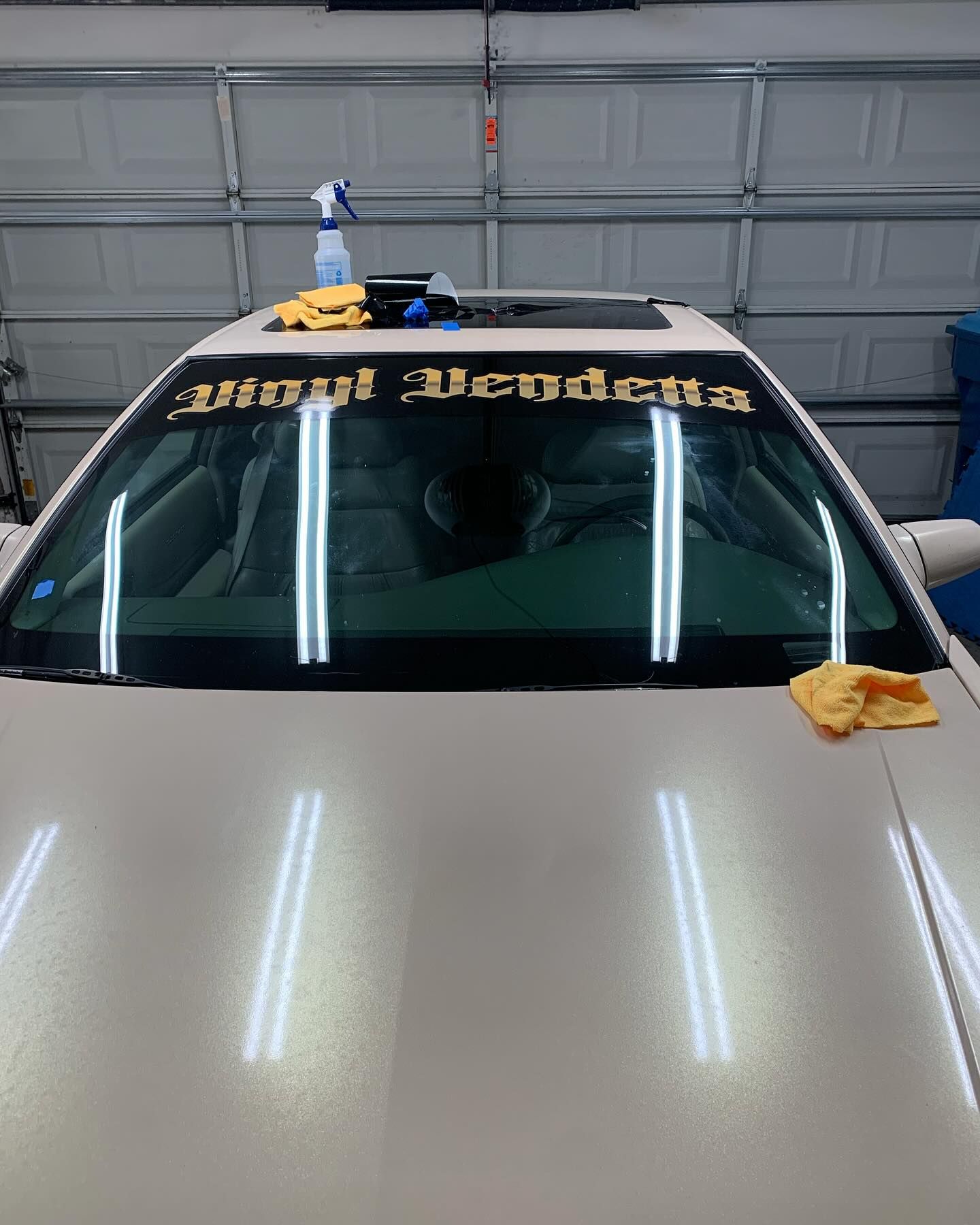 White car in a garage with gold windshield banner and a cloth on the hood