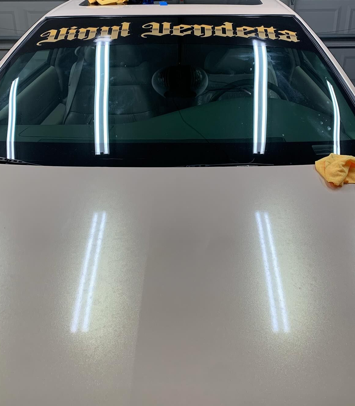 Car windshield with gold lettering and reflections of overhead lights, cloth on the hood edge