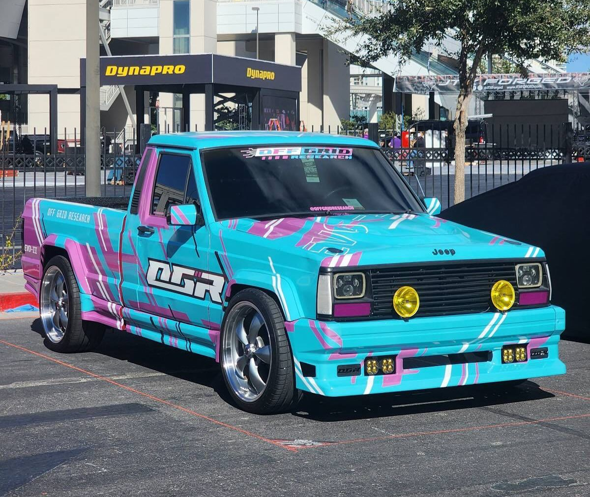 Bright pink and teal pickup truck with yellow headlights parked outdoors near a building