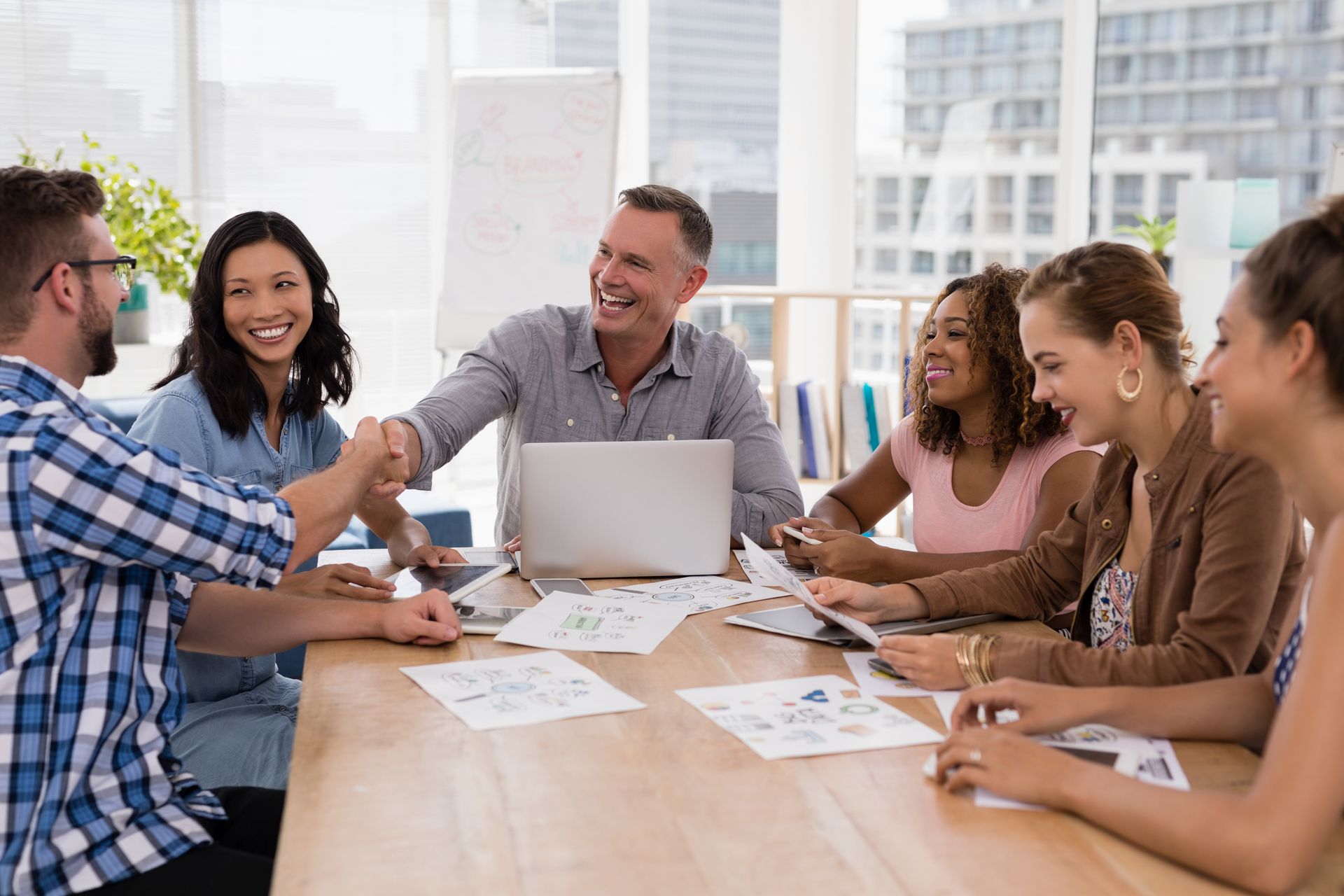 A group of people are sitting around a table shaking hands.