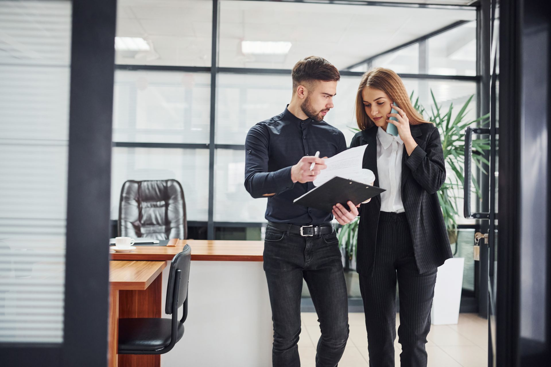 A man and a woman are standing in an office looking at a clipboard.