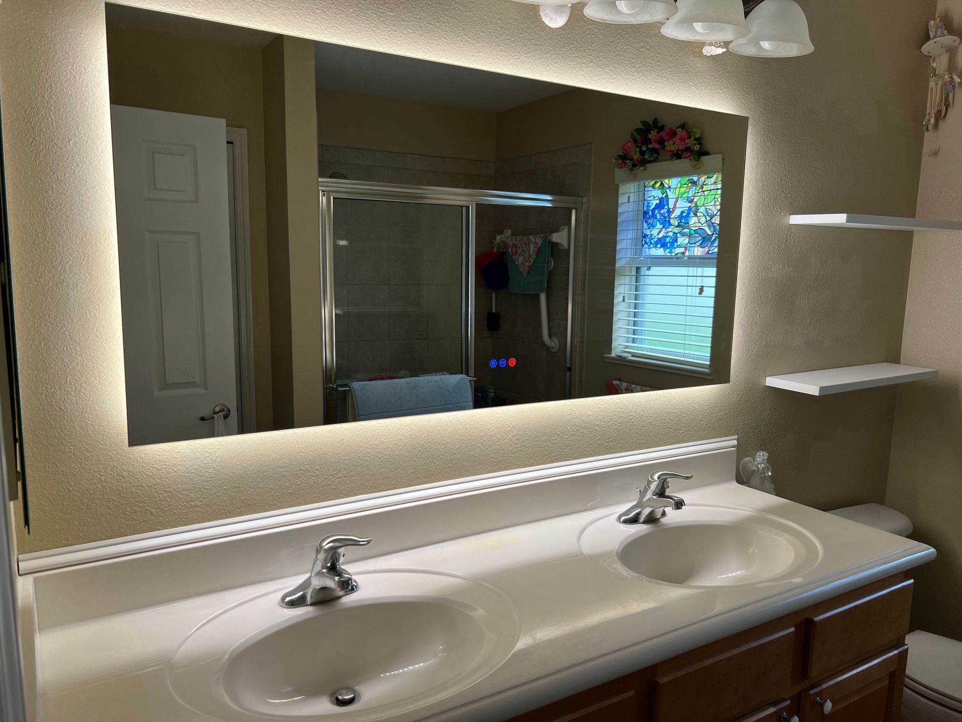 Bathroom vanity with double sinks, large mirror, and shower reflected in the mirror.