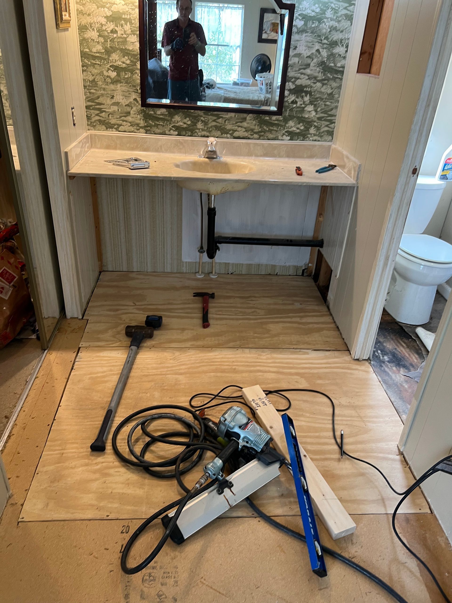 Unfinished vanity area with mirror and tools on the floor during installation or repair.