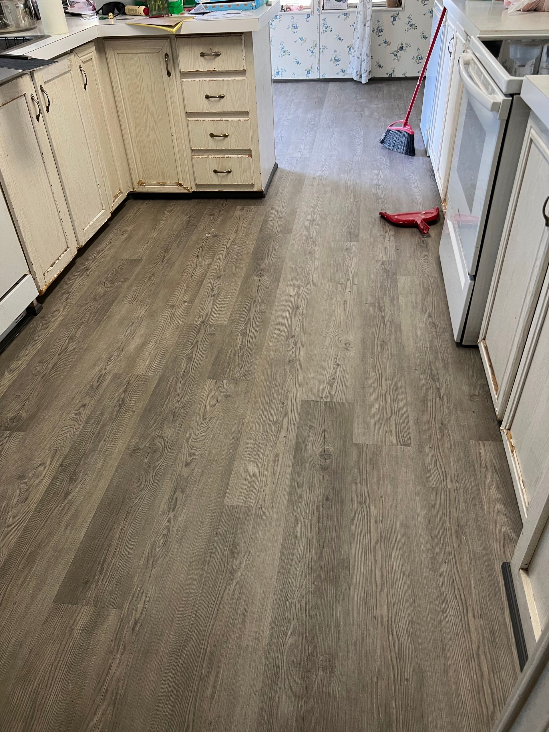 Narrow kitchen aisle with gray flooring, white cabinets, and a red broom on the right.