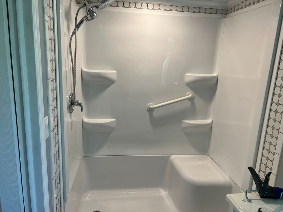 White bathtub/shower surround with built-in corner shelves and grab bars in a bathroom