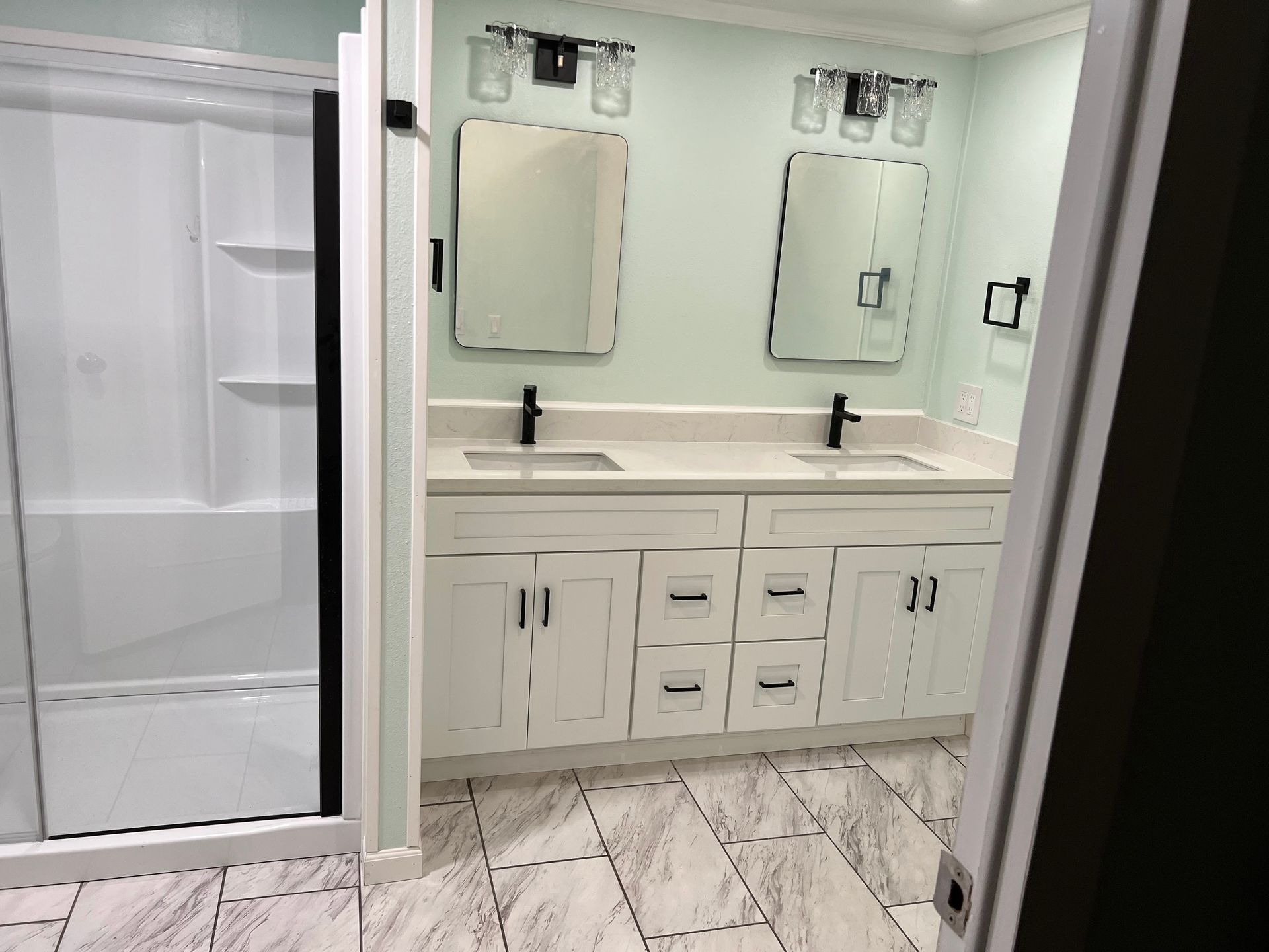 Modern bathroom vanity with double sinks, mirrors, white cabinets, and a glass shower stall