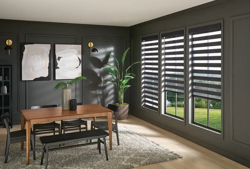 Modern dining room with wooden table, dark walls, large windows, and a potted plant near a rug.