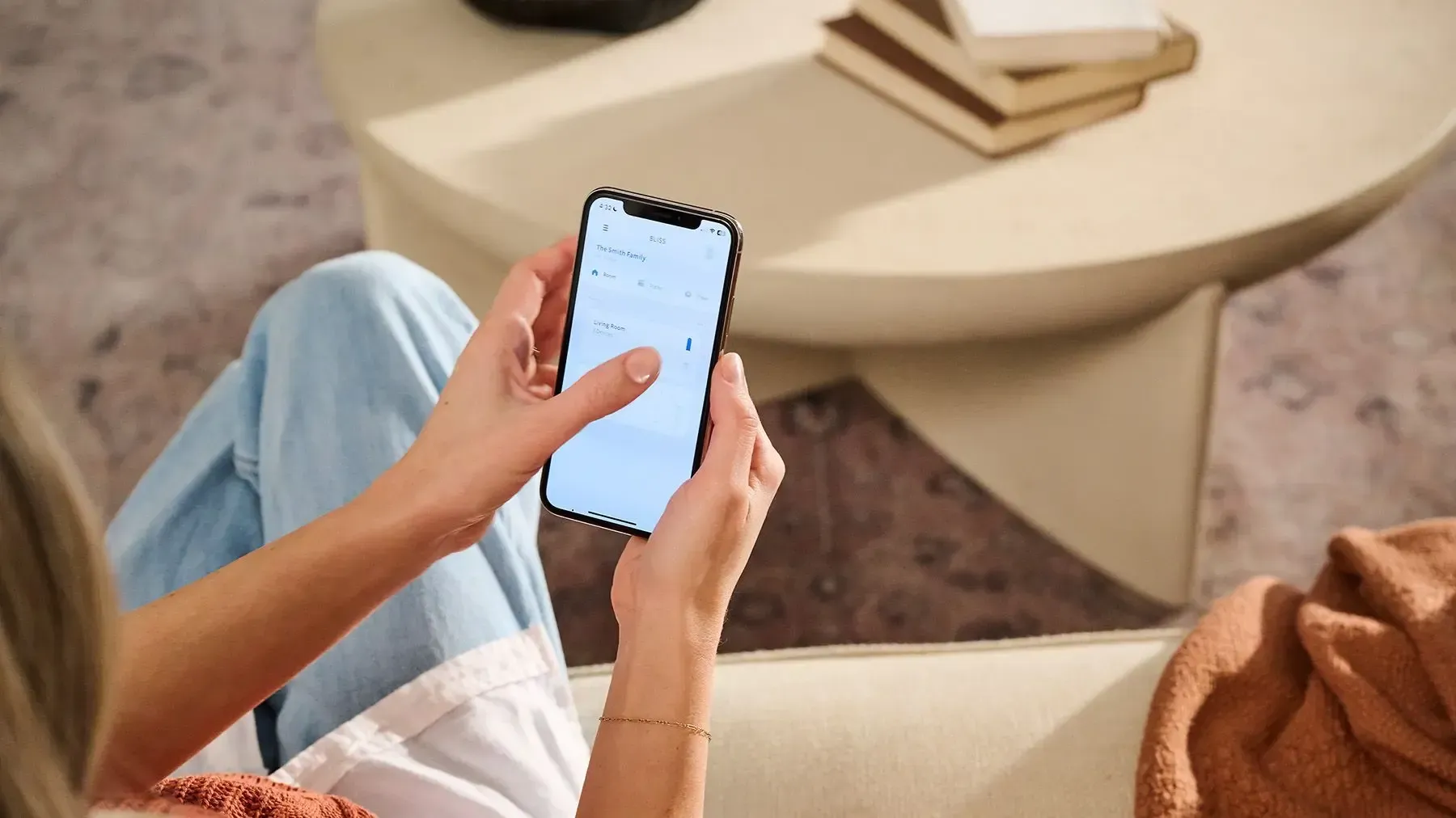 Woman sitting at a round table in a bright room, using a phone by large windows with blinds