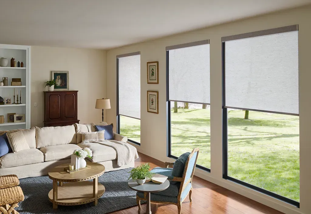 Bright living room with large windows, beige sofa, round coffee table, and view of a green yard outside