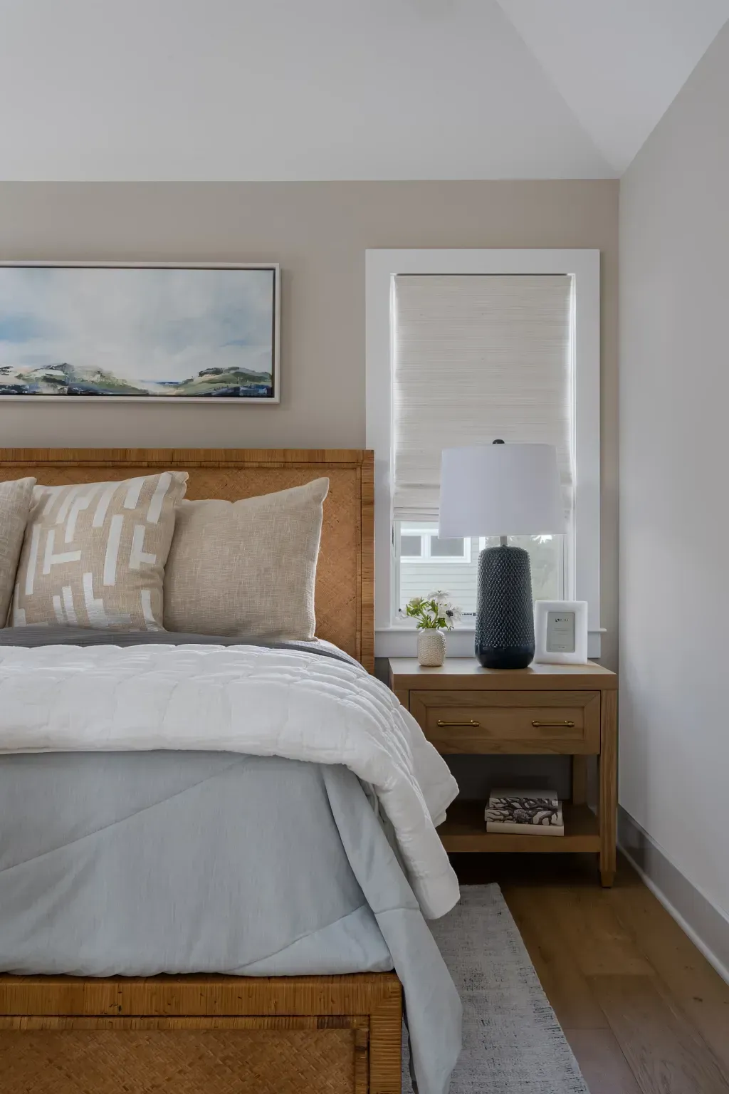 Bedroom with wooden bed, beige bedding, bedside lamp, and window with closed blinds