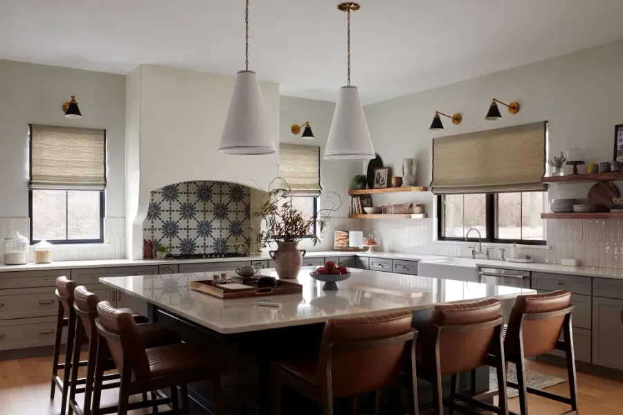 Bright kitchen with a large island, pendant lights, wood chairs, and windows with blinds