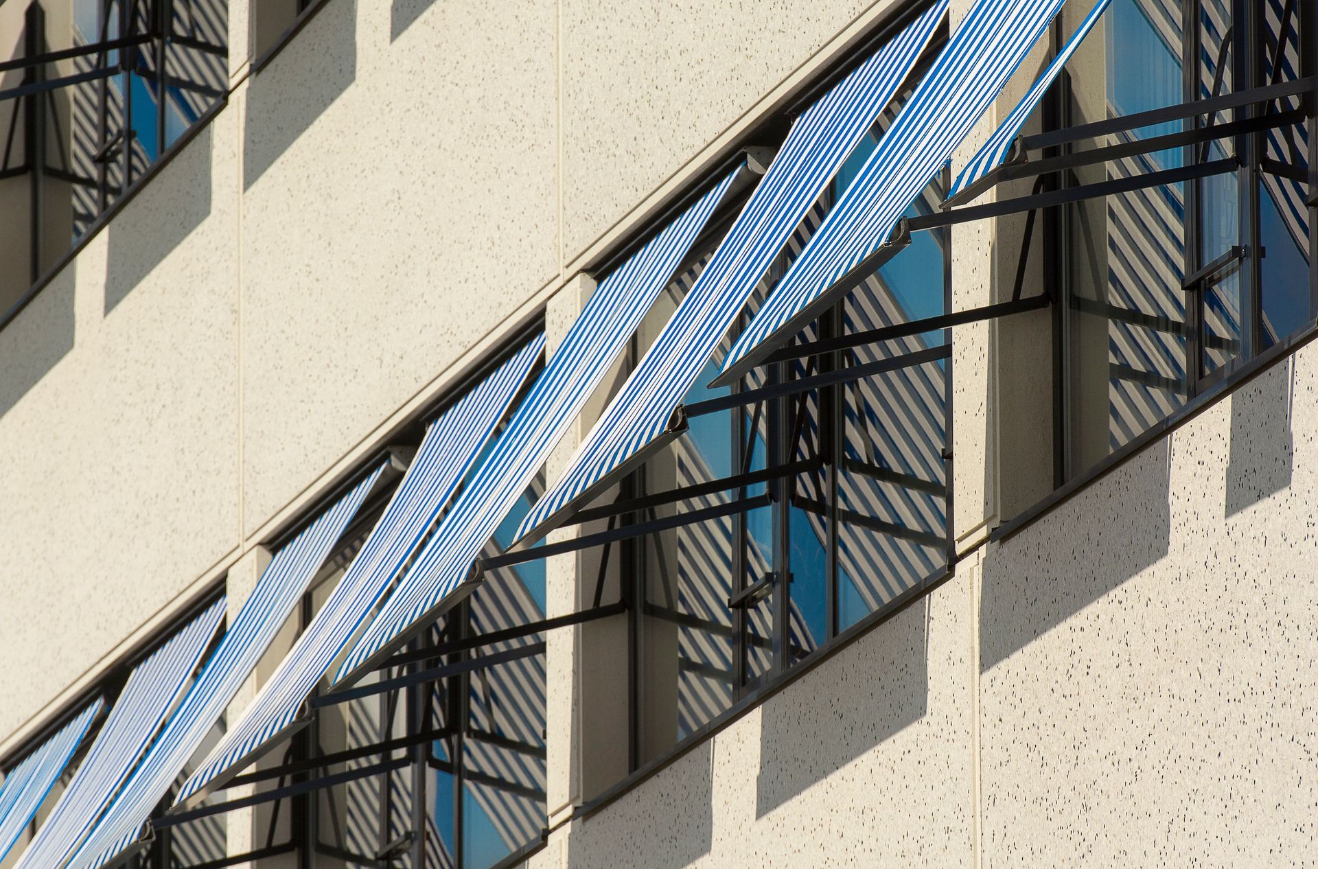 Blue-striped awnings on a beige building facade with windows and metal railings
