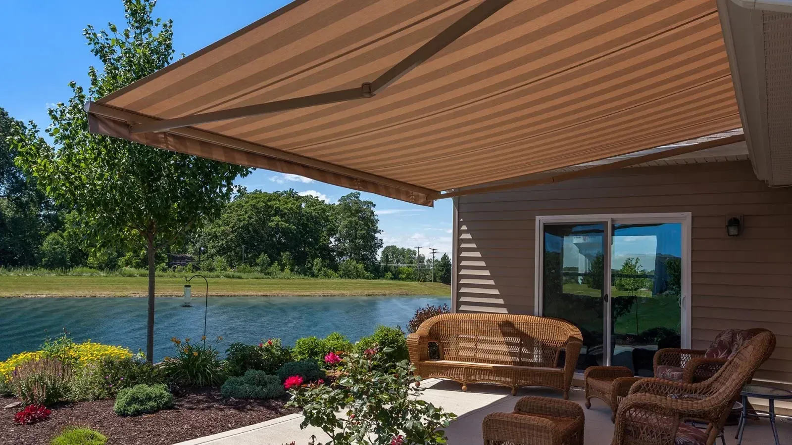 Patio with wicker chairs and tan awning overlooking a lake and trees on a sunny day
