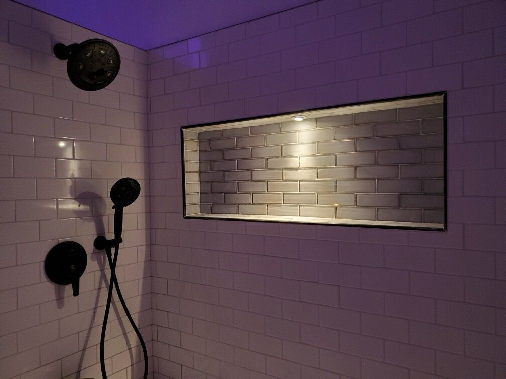 A shower with a purple light on the ceiling and a brick wall