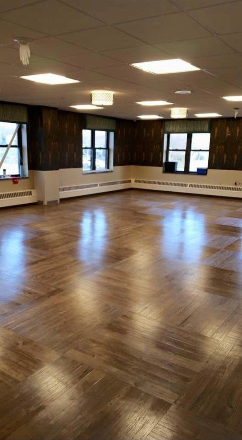 An empty, spacious room with hardwood floors, dark wallpaper, cream wainscoting, and square ceiling lights.