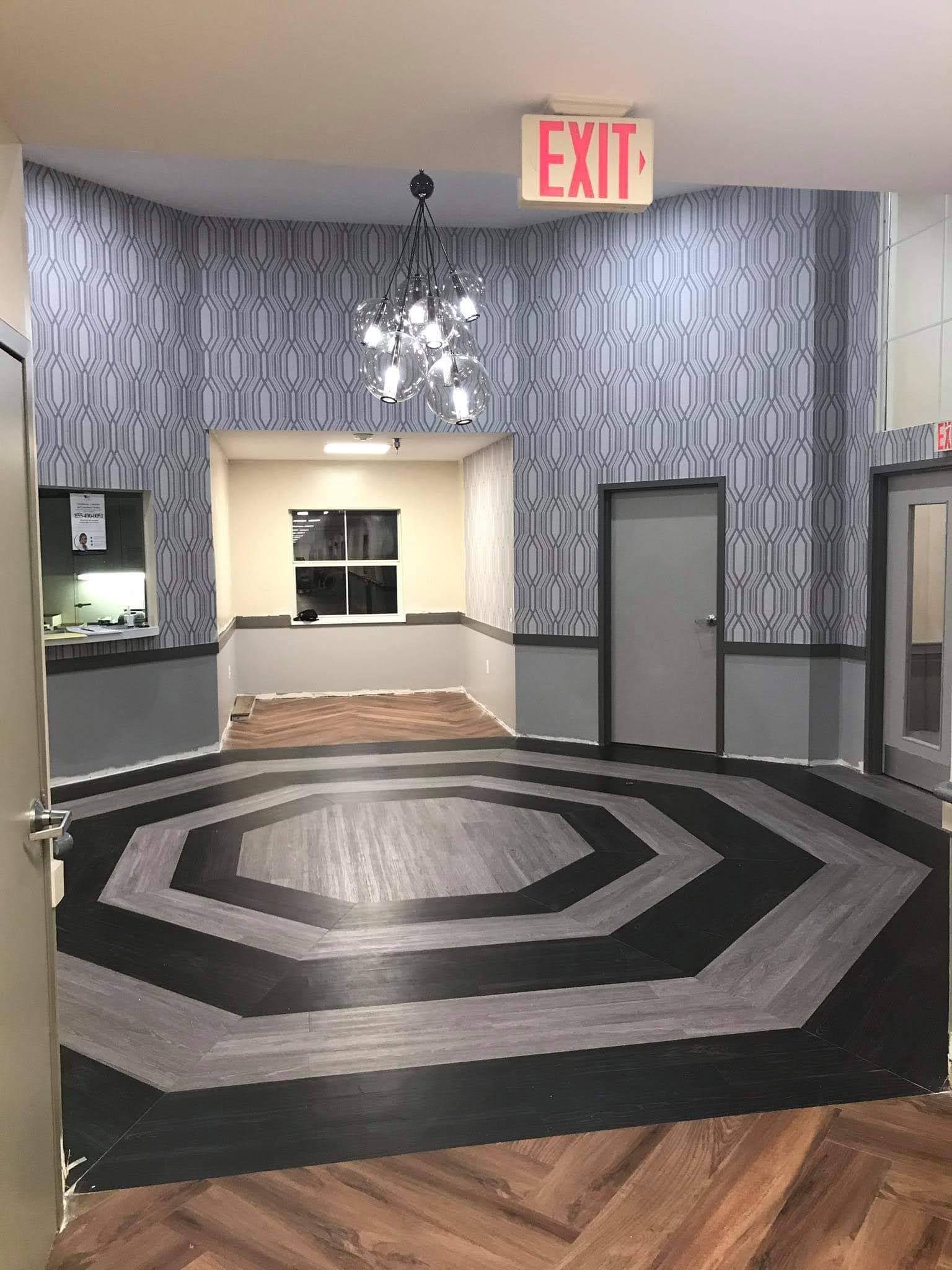 Interior view of a lobby with patterned blue wallpaper, a chandelier, and a black-and-grey octagonal patterned floor.